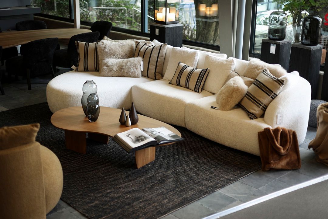 Helles, geschwungenes Sofa mit weichen Kissen und einem Couchtisch aus Holz in der Homestorys-Ausstellung.
